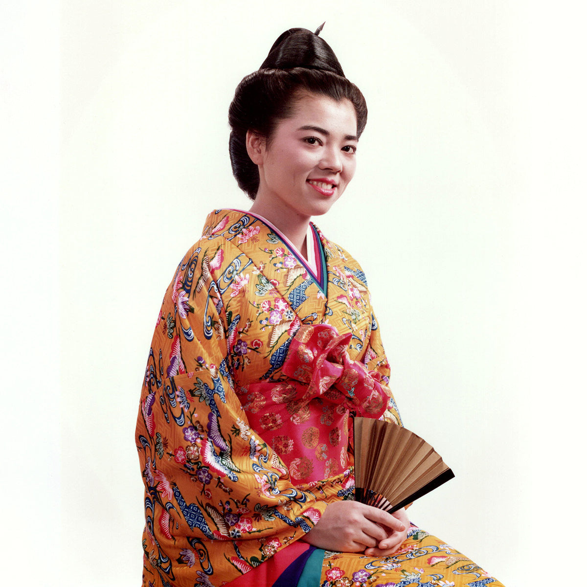 Sueko Oshimoto in a colorful Okinawa traditional outfit holding a fan on a white background