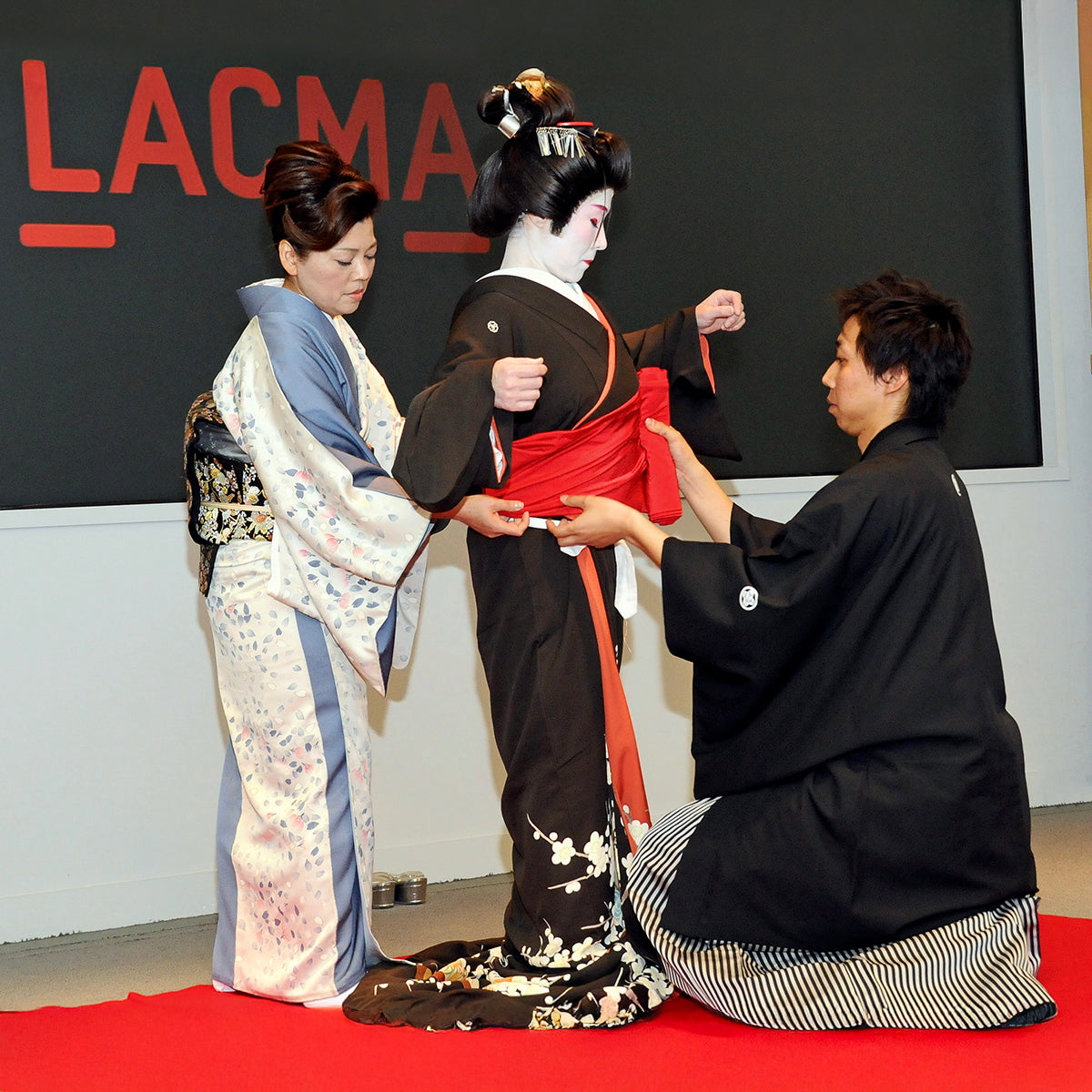 Two people in traditional Japanese attire interacting with a Geisha in front of an LACMA sign.